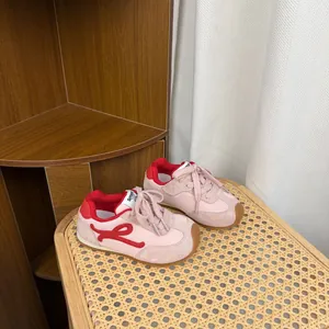Detailed view of pink and red children's retro sneakers on a textured rattan surface.