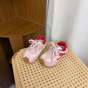 Close-up of pink and red children's retro trainer shoes placed on a stylish rattan chair