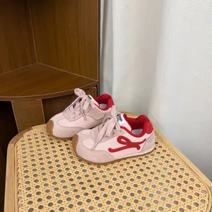 Side view of pink and red children's soft-soled sneakers on a rattan chair detail