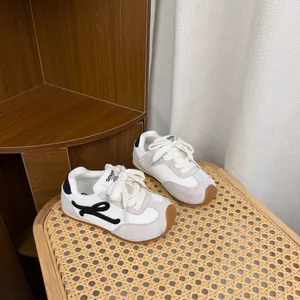 Detailed view of children's white German Trainer sneakers with gum soles on a rattan chair