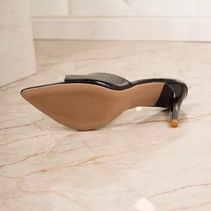Detail view of the sole and heel of a glossy black pointed-toe high-heel slide sandal.