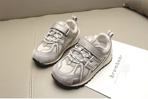 Primer plano de zapatillas grises para niños con cierre de velcro en fondo beige.