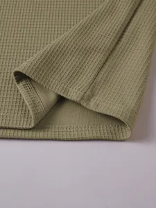 Detail close-up of olive green waffle knit fabric and hem of a men's henley t-shirt.