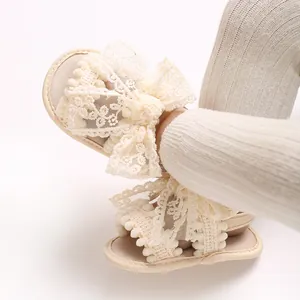 Détail de sandales crème pour bébé fille avec un nœud en dentelle délicat et des pompons
