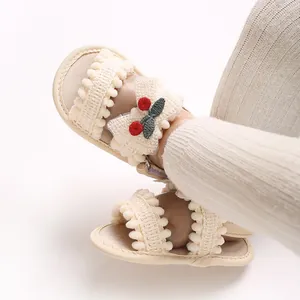 Vue détaillée de sandales crème pour bébé avec broderie cerise sur les pieds d'un bébé