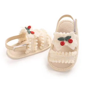 Détail de sandales bébé fille beiges avec broderie cerise, nœud en dentelle et pompons