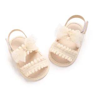Vue détaillée de sandales crème pour bébé avec d'élégants nœuds en dentelle et pompons