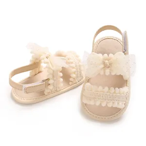 Vue détaillée de sandales beiges pour bébé fille avec nœud en dentelle et pompons