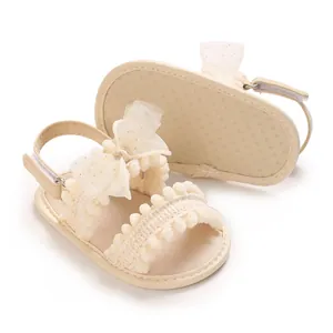 Vue détaillée de sandales d'été beiges pour bébé avec nœud en maille et bordure à pompons.