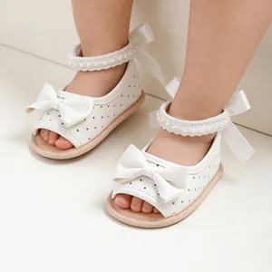 Gros plan de sandales blanches pour bébés filles avec nœuds décoratifs et perles.