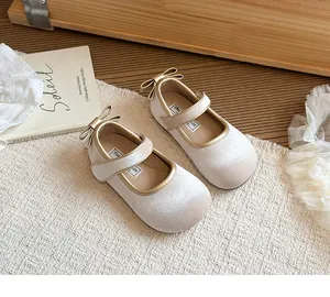 Primo piano di scarpe Mary Jane in velluto beige per bambina con fiocchi dorati.
