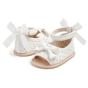 Détail de sandales blanches pour bébés filles avec nœuds en ruban et brides en perles