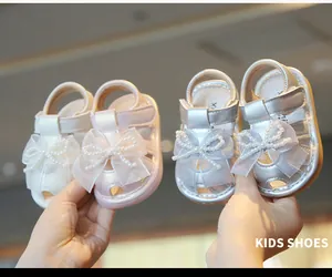 Close-up detail of baby girl summer sandals with pearl bows in cream and silver colors