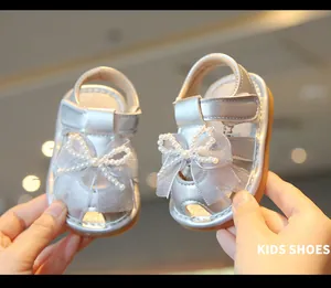Close-up of silver baby girl sandals with pearl bow and soft sole detail