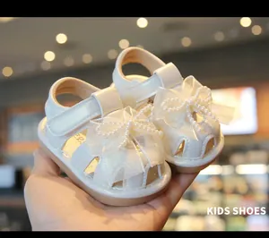Close-up of white baby girl sandals featuring elegant pearl butterfly bows and soft soles