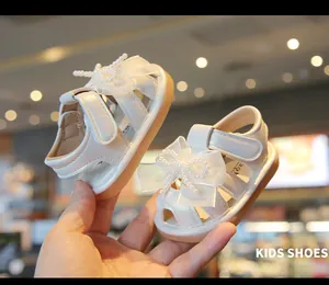 Close-up view of white baby girl princess sandals featuring elegant pearl bow details
