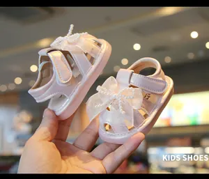 Close-up view of pink baby girl sandals featuring elegant pearl bow details held by hand