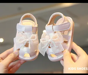 Detail view of pink baby girl sandals with elegant pearl bow accents and soft nonslip soles.