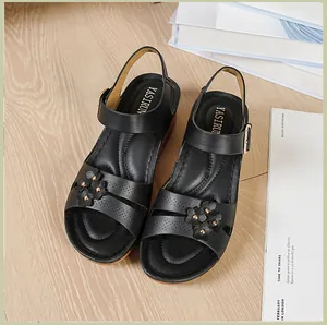 Detailed view of black wedge sandals featuring decorative flowers and gold studs.
