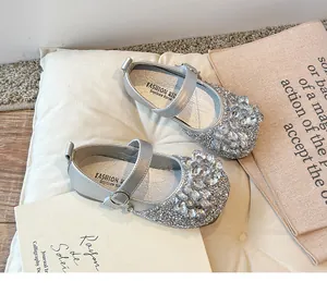 Détail de chaussures Mary Jane argentées avec strass brillants sur un coussin blanc.