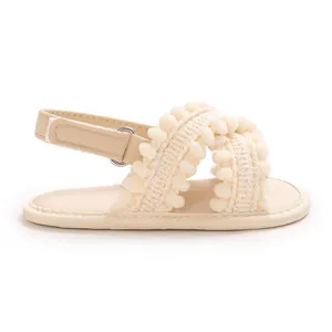 Detalle de sandalias beige para bebé con correas de pompones y cierre de velcro