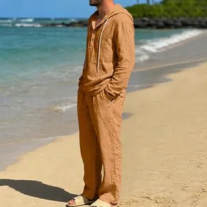 Herren Leinen-Set mit Kapuzenpullover und langer Hose in Ingwergelb am Strand seitlich.