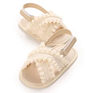 Sandalias suaves color crema para bebé niña con pompones y correa de talón ajustable.