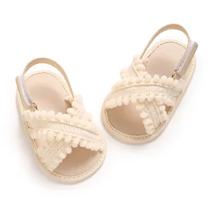 Detalle de sandalias suaves beige para bebé niña con tiras cruzadas de pompones