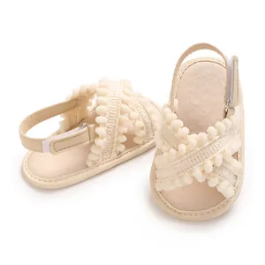 Primer plano de sandalias cómodas para bebé en color crema con tiras de pompones