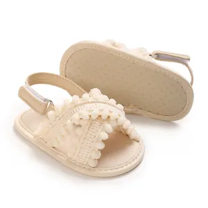 Primer plano de sandalias suaves crema para bebé con correas cruzadas de pompones.