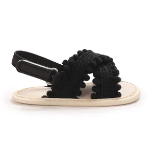 Vista lateral de sandalias negras suaves para bebé con flecos de pompones y velcro.