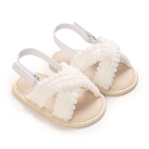 Detalle de sandalias blancas para bebé con correas cruzadas de pompones y suelas blandas