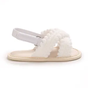 Vista lateral de sandalias blancas para bebé niña con pompones y cierre de velcro