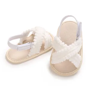 Primer plano de sandalias blancas para bebé con pompones y correas ajustables.
