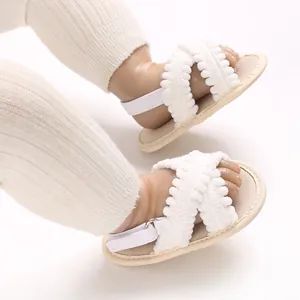 Detalle de sandalias blancas para bebé con tiras de encaje y pompones para niñas.