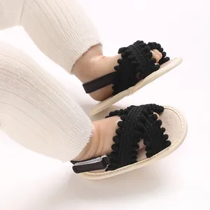 Primer plano de sandalias de bebé negras con pompones y suela blanda antideslizante