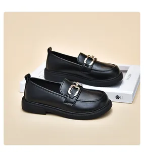 Elegante schwarze Mädchen-Loafer mit goldener Metallschnalle auf beigem Hintergrund.