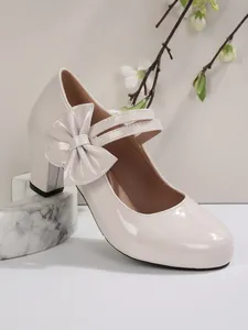 Vista laterale di scarpe crema in vernice con tacco largo e fiocco