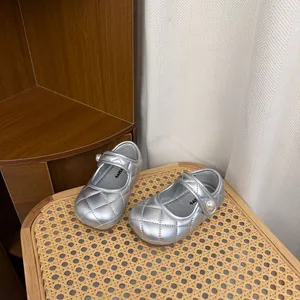 Silver quilted children's Mary Jane shoes with pearl buckle detail on a rattan stool