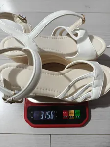 Sandali bianchi con zeppa e plateau dal peso di 315,6 g su una bilancia digitale.