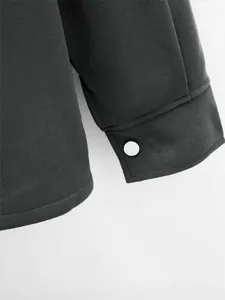 Gros plan montrant les coutures fines et le bouton pression blanc d'une veste grise