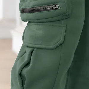 Detail shot of men's green cargo pants showing zipper and flap pocket texture.