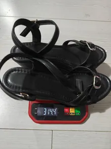 Vista dettagliata dei sandali con zeppa neri su una bilancia che segna 314,4 grammi.