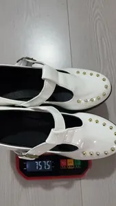 Gewichtsweergave van witte lakleren Mary Janes met gouden studs.