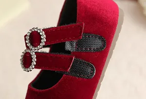 Nahaufnahme der Doppelriemen mit Strass-Schnallen an roten Samt-Mary-Jane-Schuhen.