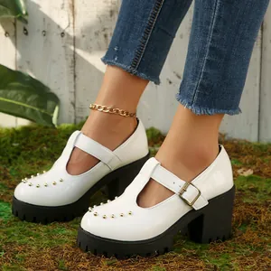 Gedetailleerde weergave van witte Mary Jane-hakken met plateau en gouden studs op mos