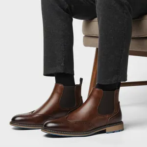 Nahaufnahme von braunen Chelsea Boots mit Brogue-Muster und dunkler Hose im Studio.