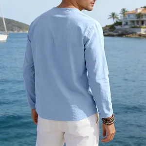 Back view of a men's loose light blue linen casual long sleeve t-shirt in a coastal setting
