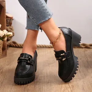 Detail van zwarte loafers met platform en blokhak met metalen gesp op houten vloer