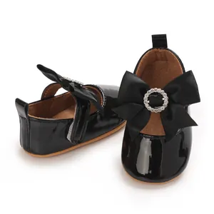Detail of shiny black baby girl shoes with large decorative bow and rhinestone ring.